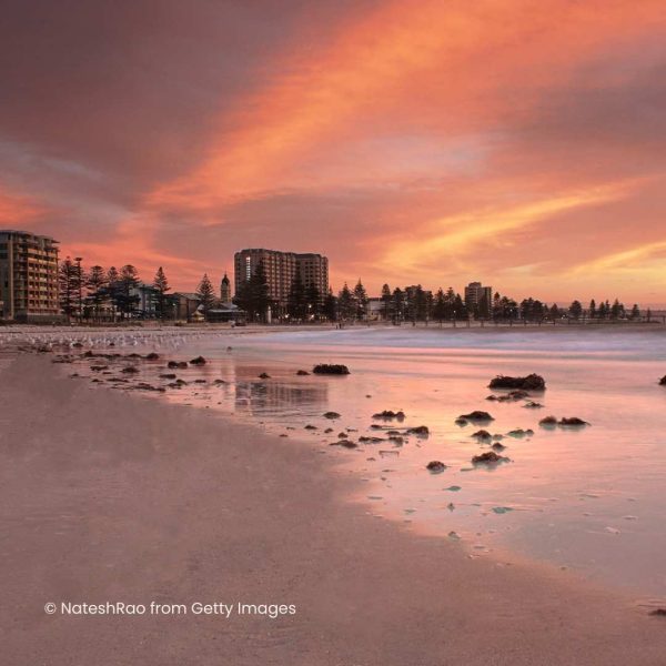 Orange sky relfected off shallow beach water. The city can be seen in the distance